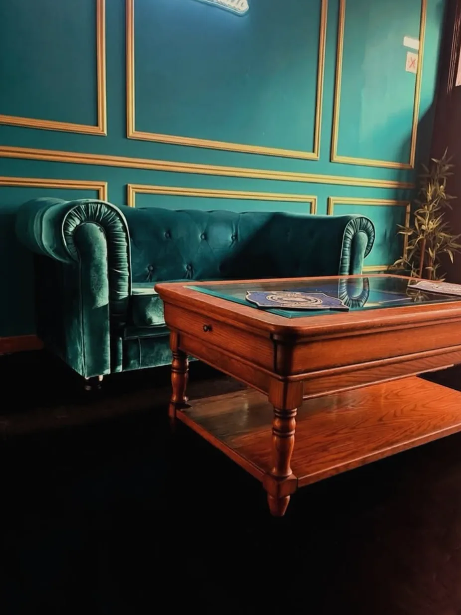 Sofá Chesterfield de terciopelo verde junto a la pared panelada con molduras doradas del salón